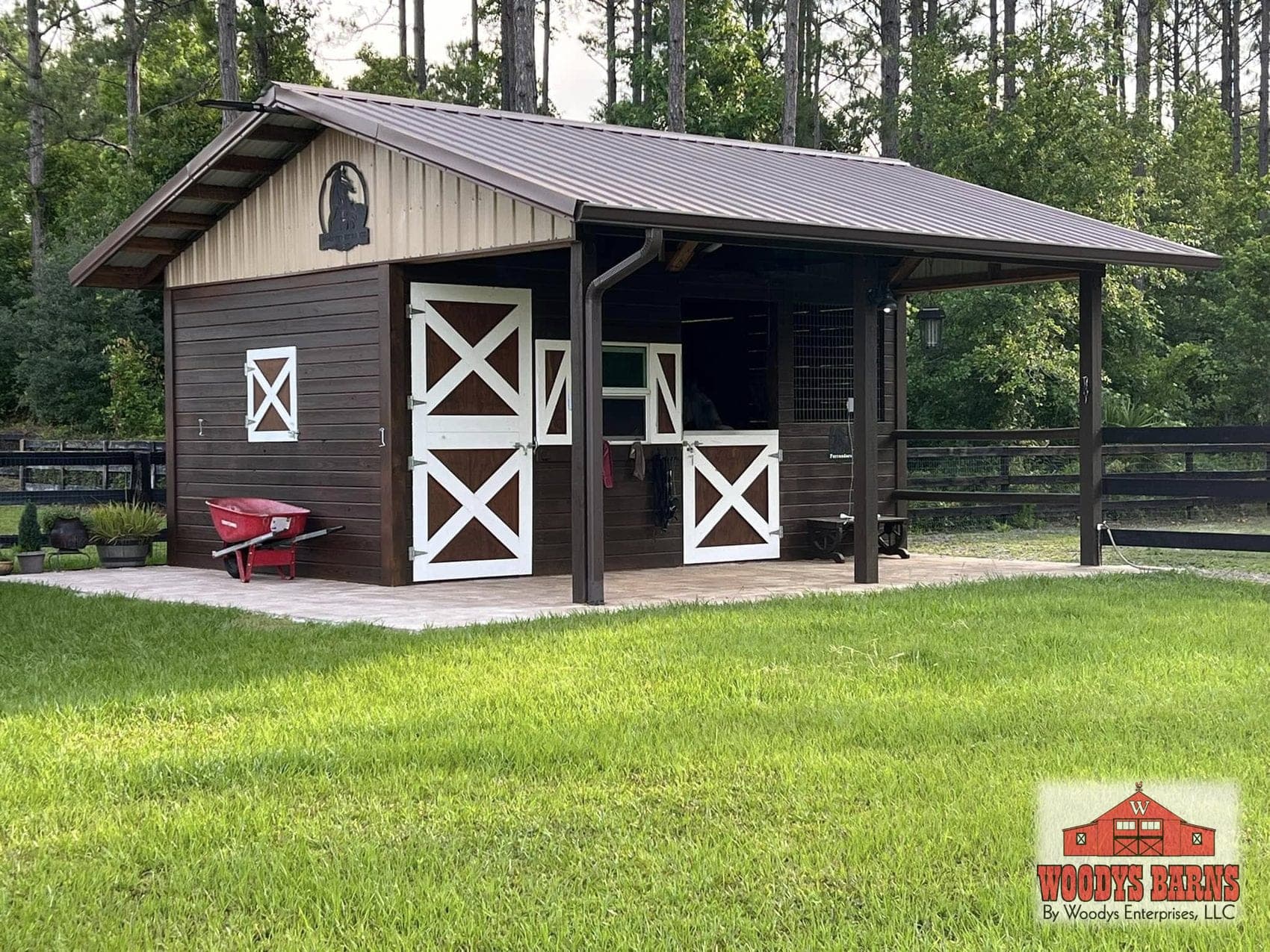 The Ramos shed row barn, dark brown with white cross buck stall doors under a covered overhang, built by Woodys Barns in Florida