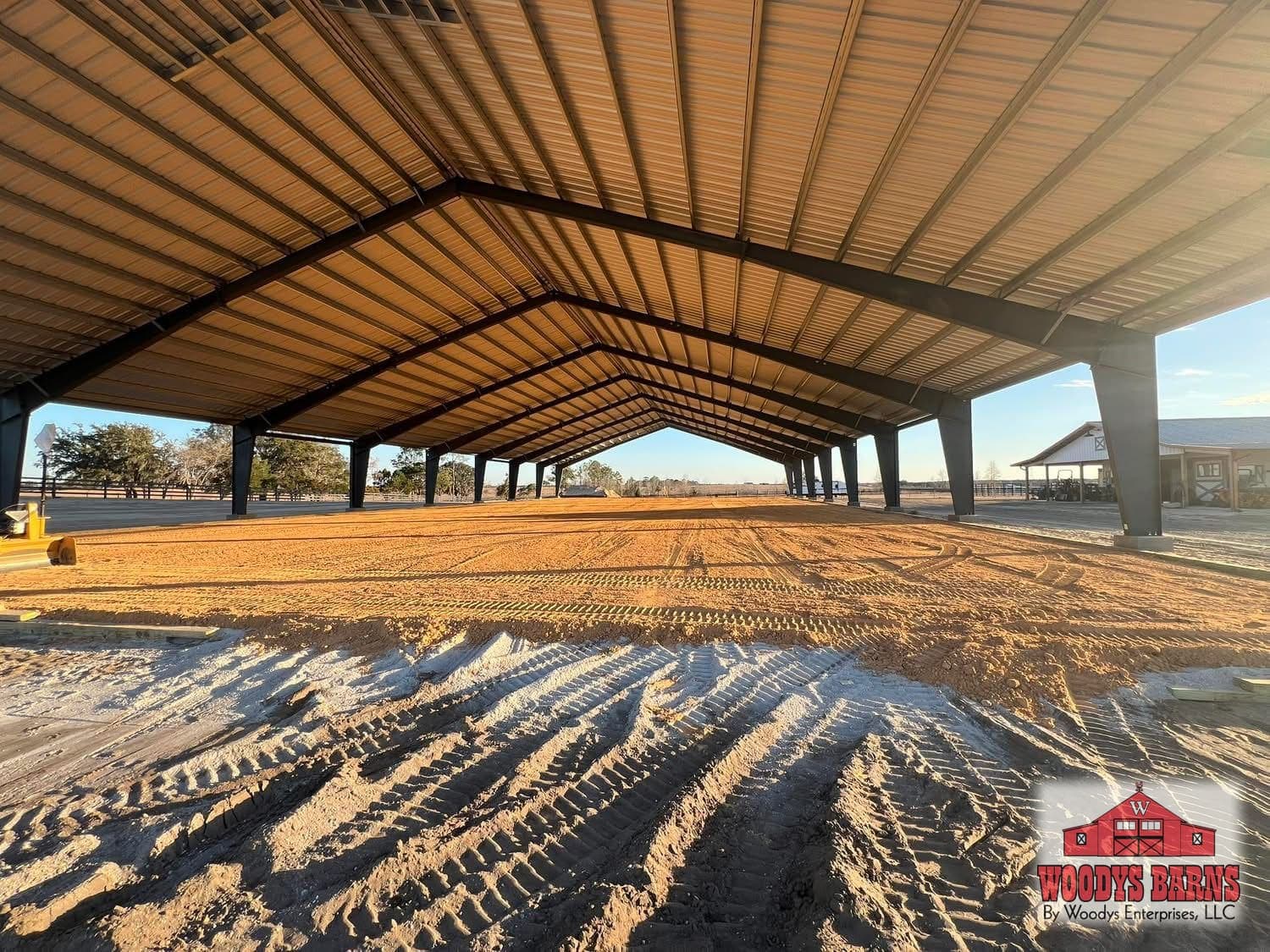Clear span red iron arena frame in golden evening light, built by Woodys Barns in Florida