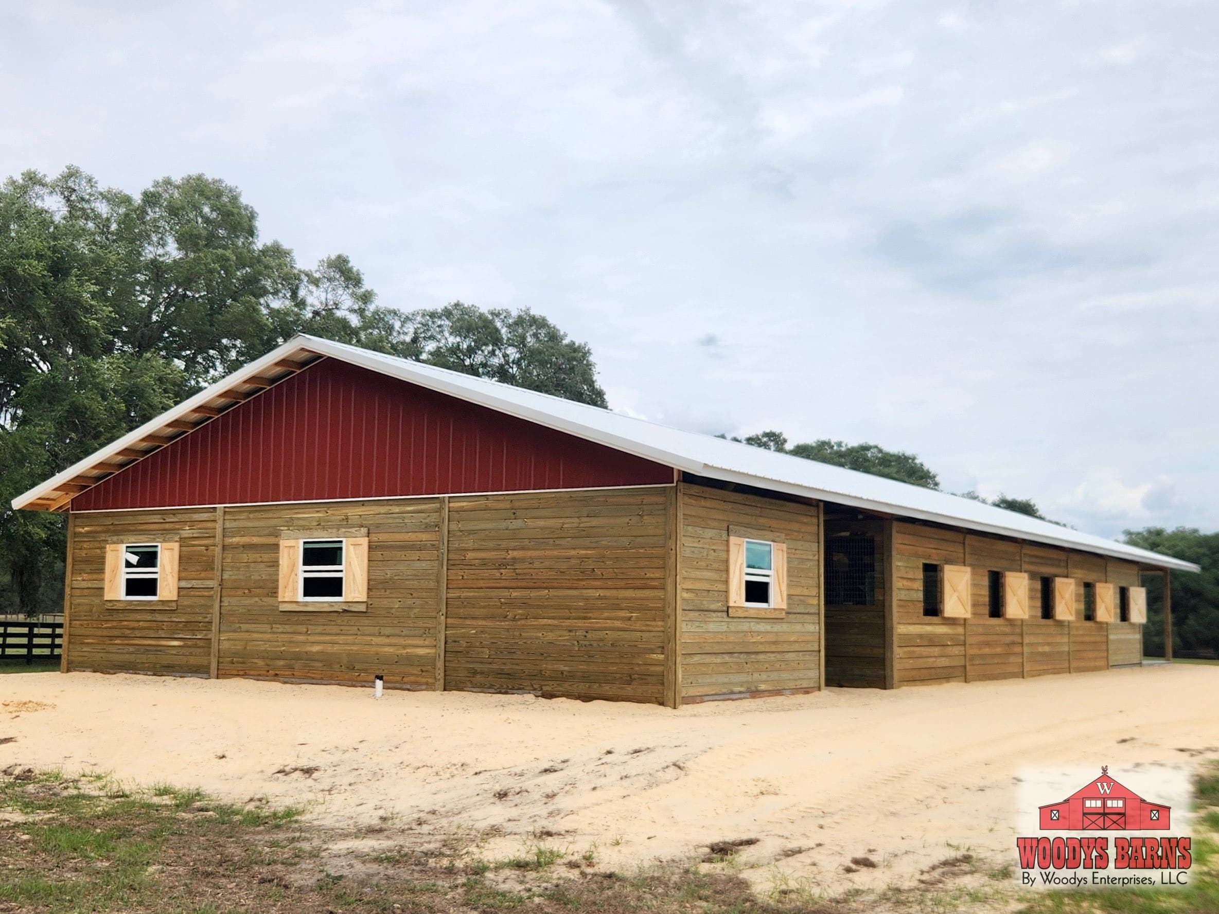 A long Woodys Barns horse barn with a Rustic Red gable under a Galvalume roof, built on Florida sand