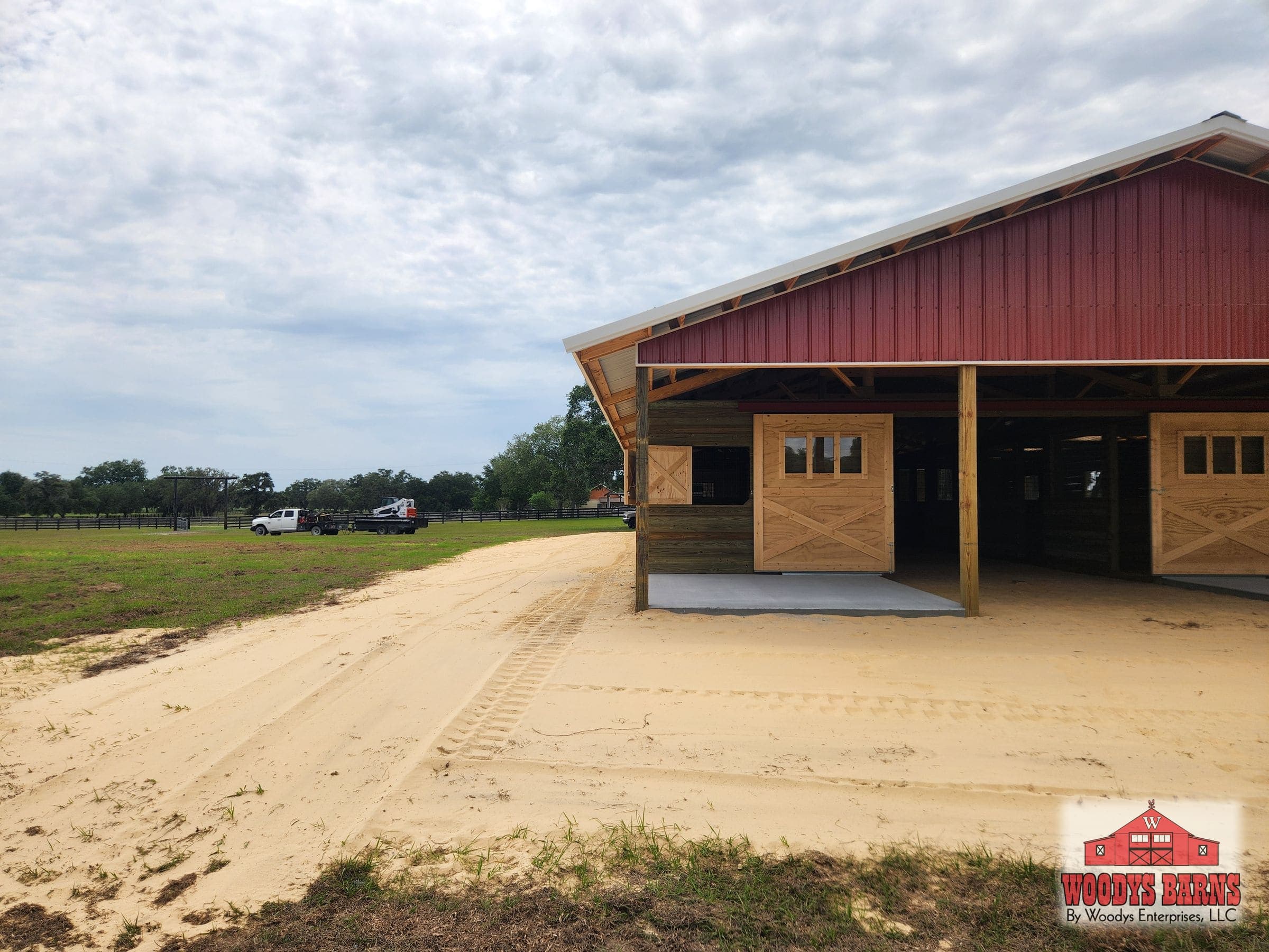 Center aisle horse barn with a Rustic Red gable under a Galvalume roof, built by Woodys Barns on a Florida farm